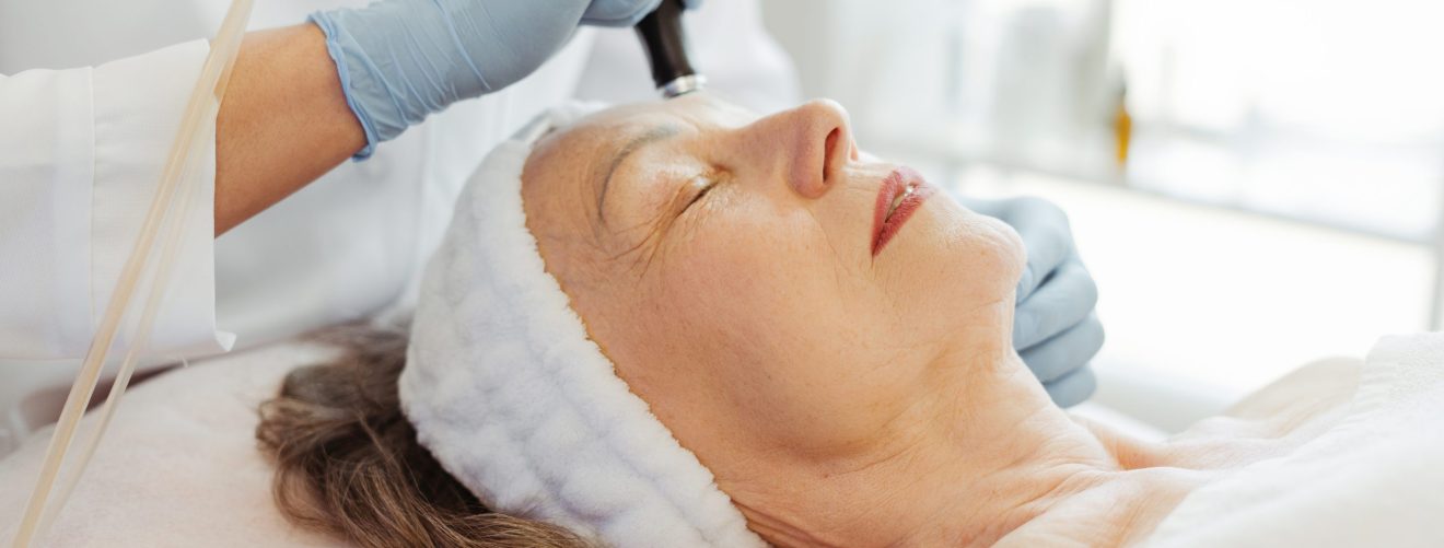 Closeup professional beautician in gloves conducts vacuum cleaning and polishing face skin of senior, mature woman in cosmetology clinic. Moisturizing and rejuvenating procedures. Cosmetology concept
