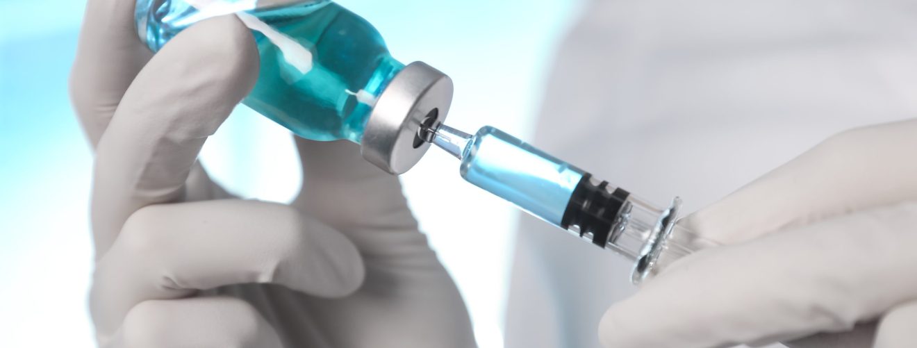 Doctor filling syringe with vaccine from vial on blurred background, closeup